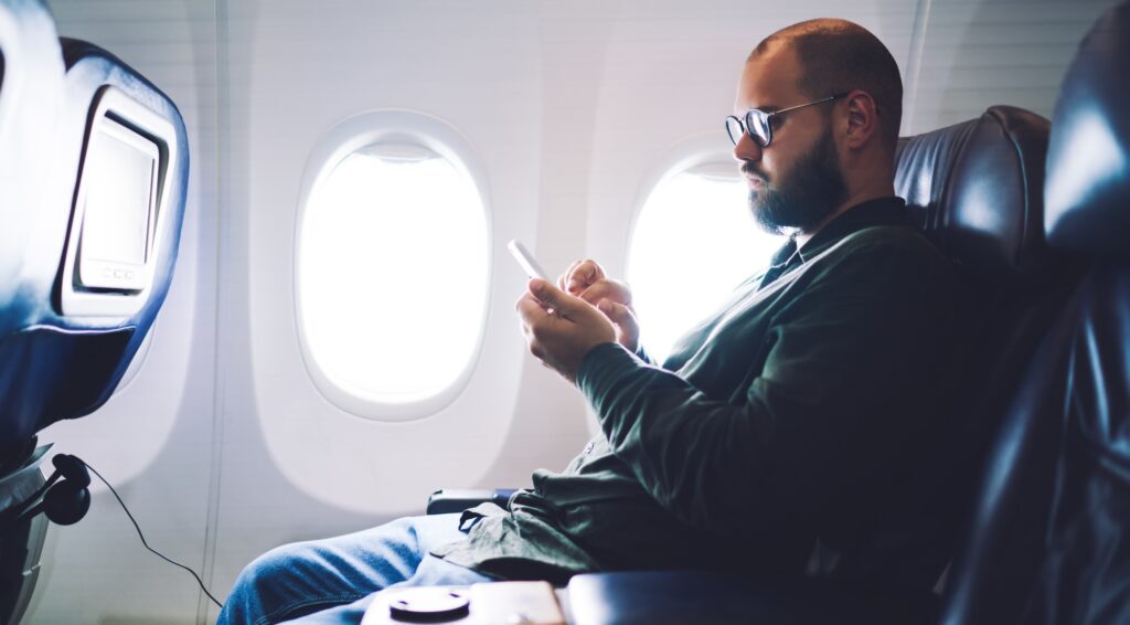 Male on plane checking smartphone during flight