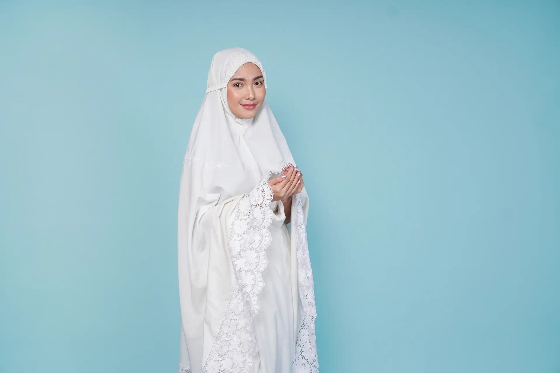 Serious young Asian Muslim woman wearing prayer gown praying pose with hands.
