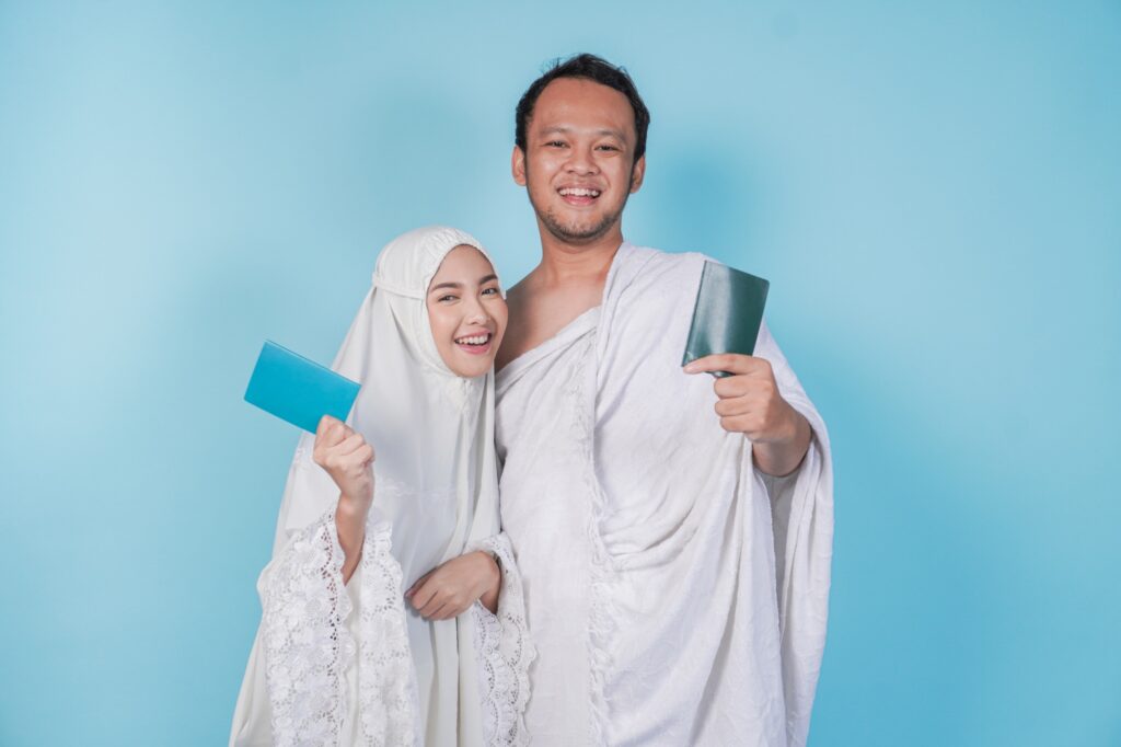 Smiling young Asian Muslim couple wearing ihram and prayer gown holding passport. Hajj concept.